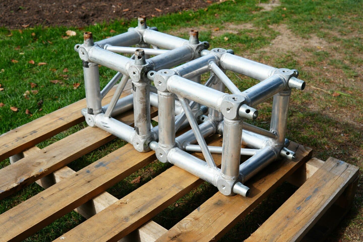 Traversenelemente aus Aluminium liegen auf einer Holzpalette im Gras