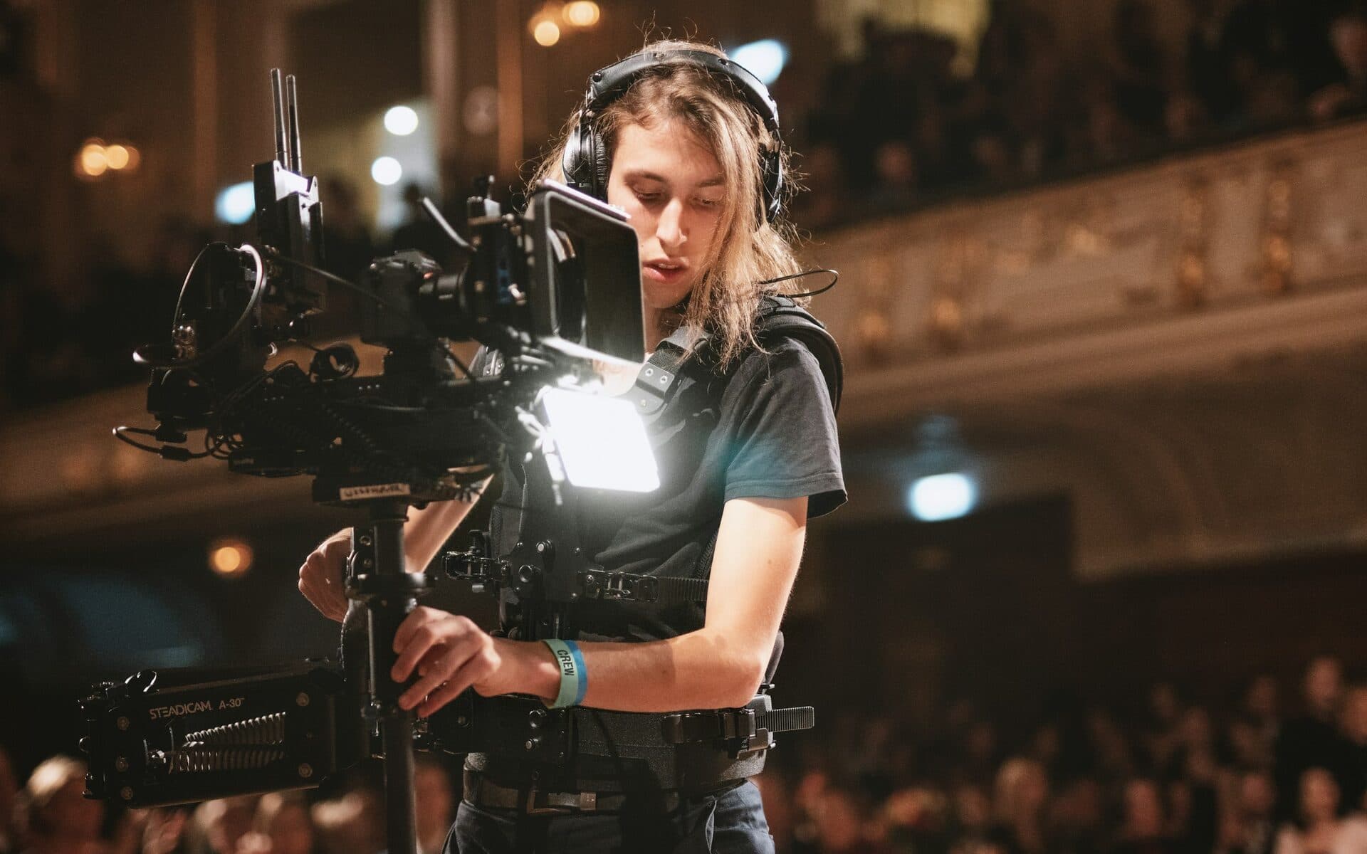 Person mit Kopfhörern filmt mit einem Kamera-Rig bei einer Veranstaltung im Saal
